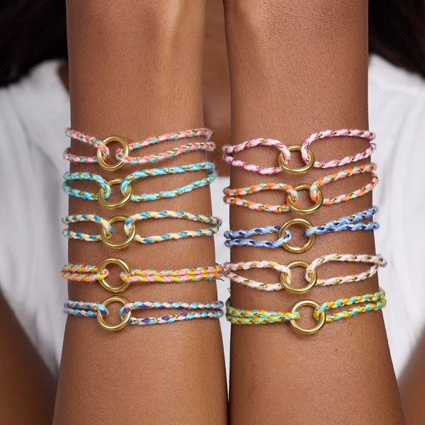 Multicolored braided bracelets with gold loops on a person's wrist against a white background